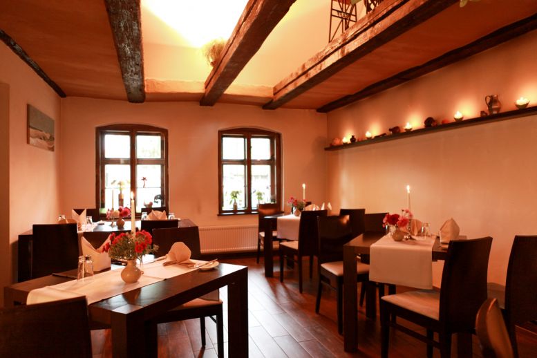 Restaurant Philippsthal Innenraum, rustikale Balken an der Decke mit Lehm verpuzte Wände in einerm warmes Weiß, Stilvoll Gedeckte Tische mit Blumenvasen.