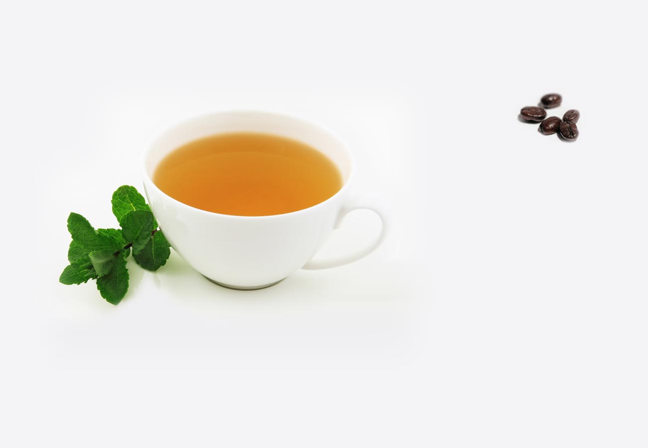 Getränkekarte - Heißgetränk, eine Tasse heller Tee mit frischer Minze und ein paar Kaffeebohnen auf einem weißem Tisch