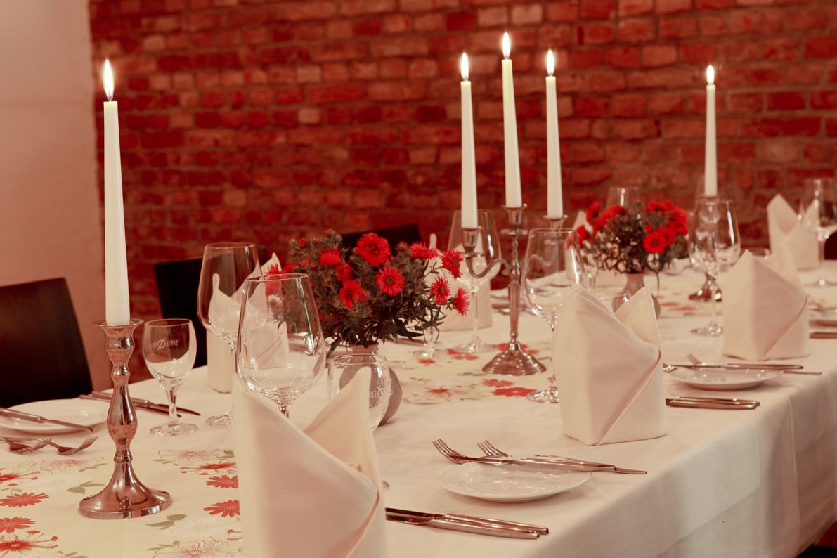 Gastraum mit warmer Beleuchtung und mehreren tischen, Auf den tischen stehen brennende Kerzen.